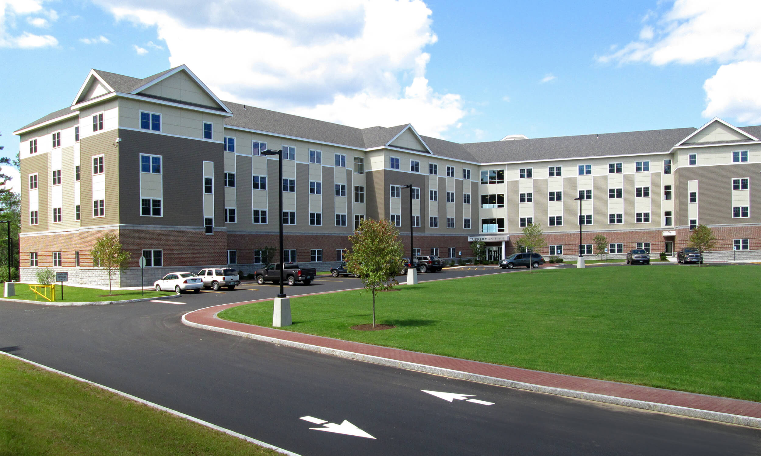 Exterior view of a college campus building with light brown and white facade and a green courtyard area in front.