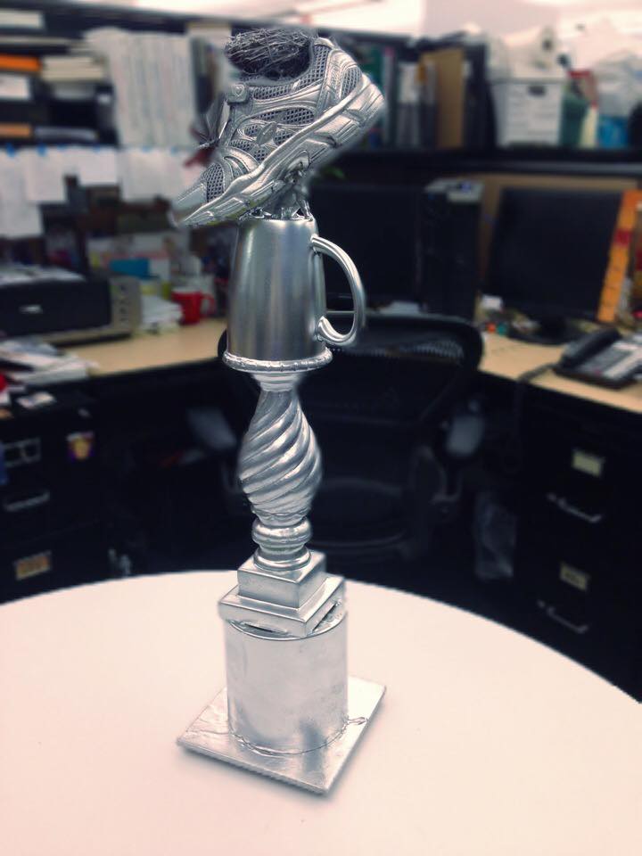 Closeup photo of a silver awards trophy that features an athletic shoe on top.