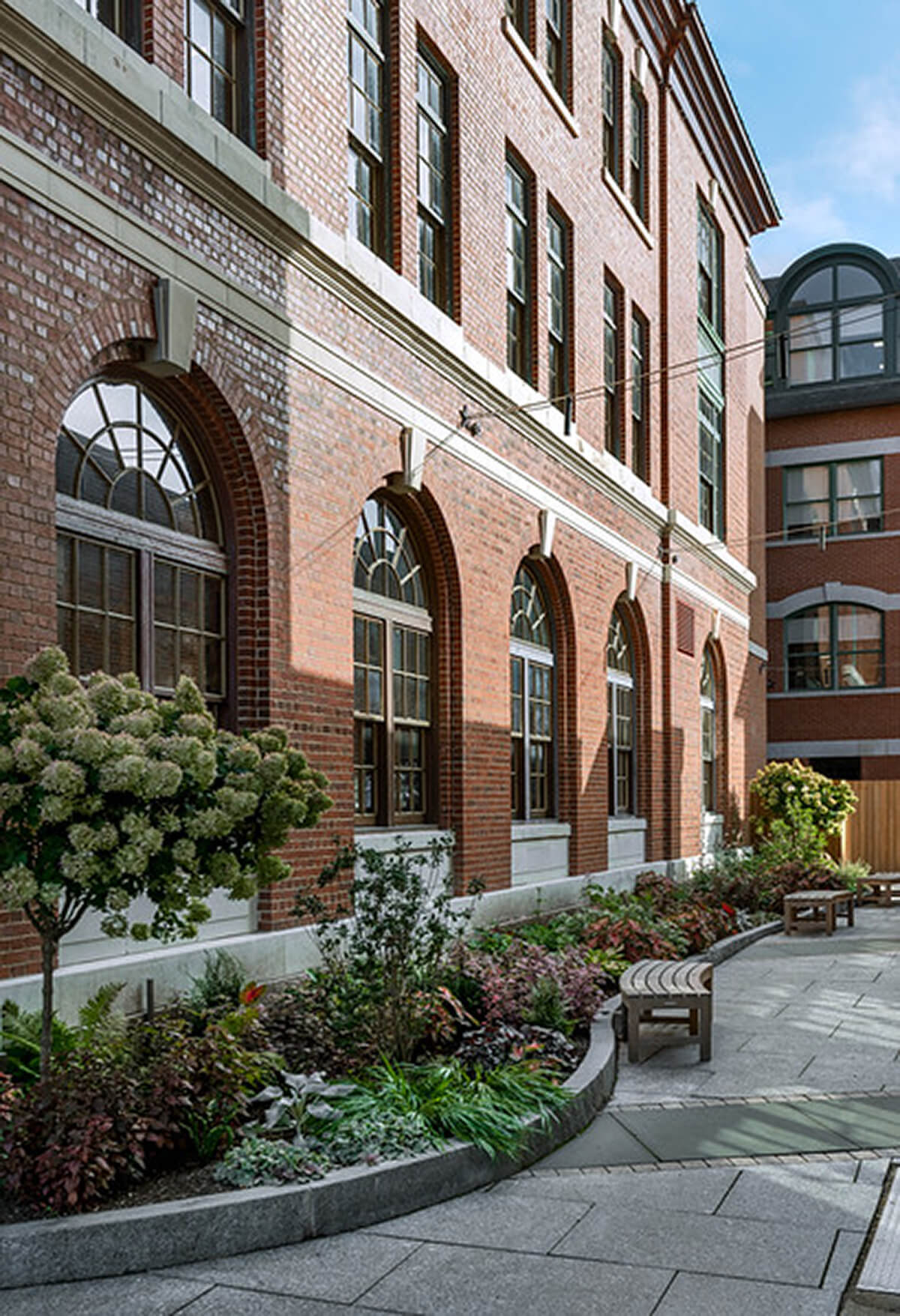 Exterior daytime photo showing the facade edge of a historical brick building with planters beautifying the edge.