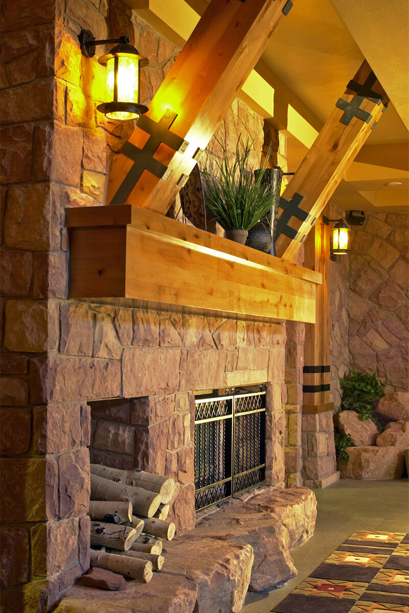 Interior photo of a stone fireplace with stacked wood next to it in a lobby area of a ski resort.