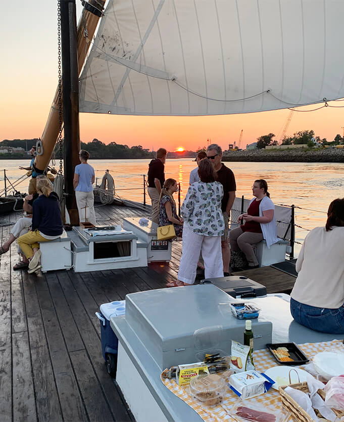 Photo taken of staff members socializing on the deck of a small boat with a beautiful sunset view in the background.