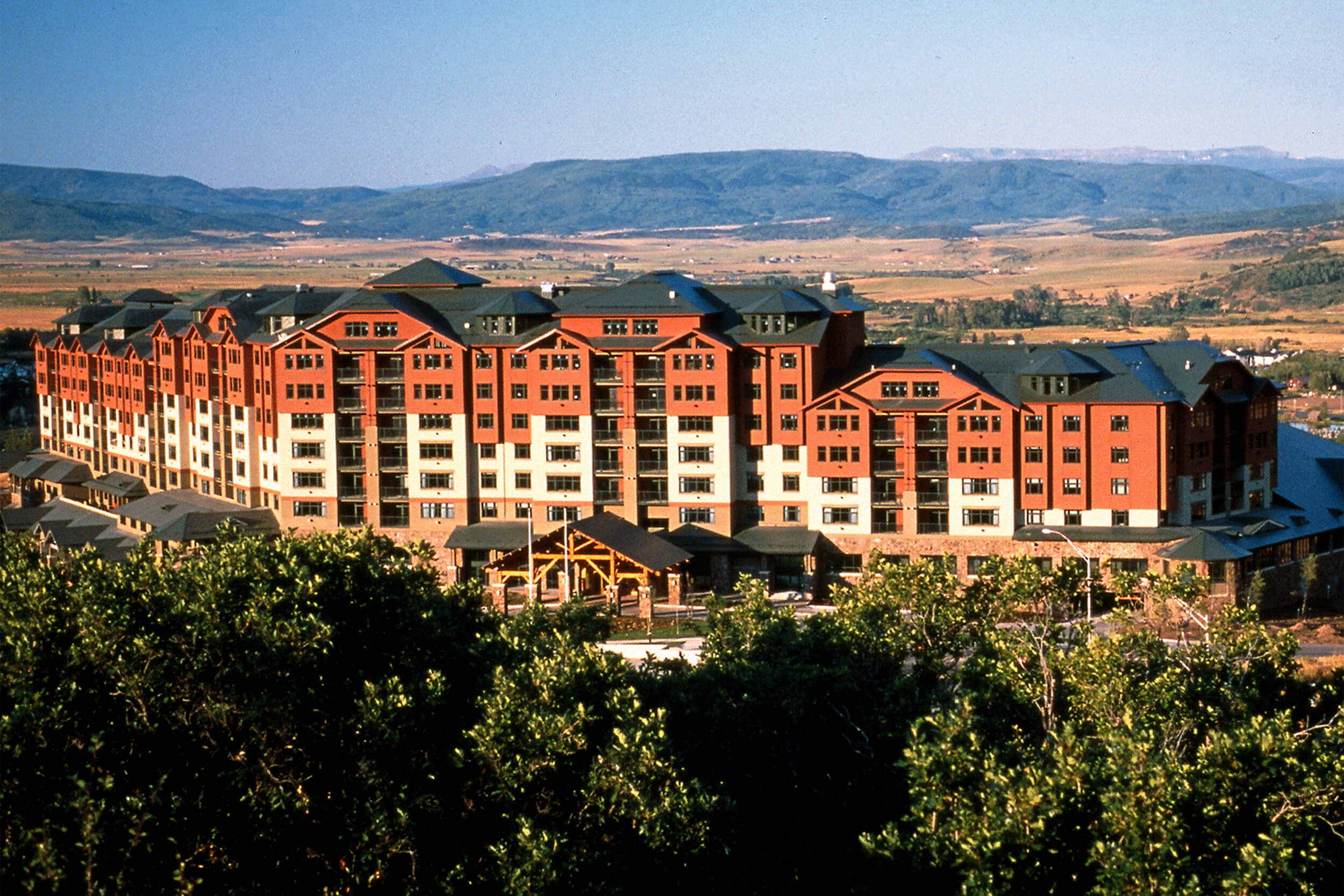Exterior daytime view of a ski resort with mountains in the background. The multi-unit building has a brown and white facade.