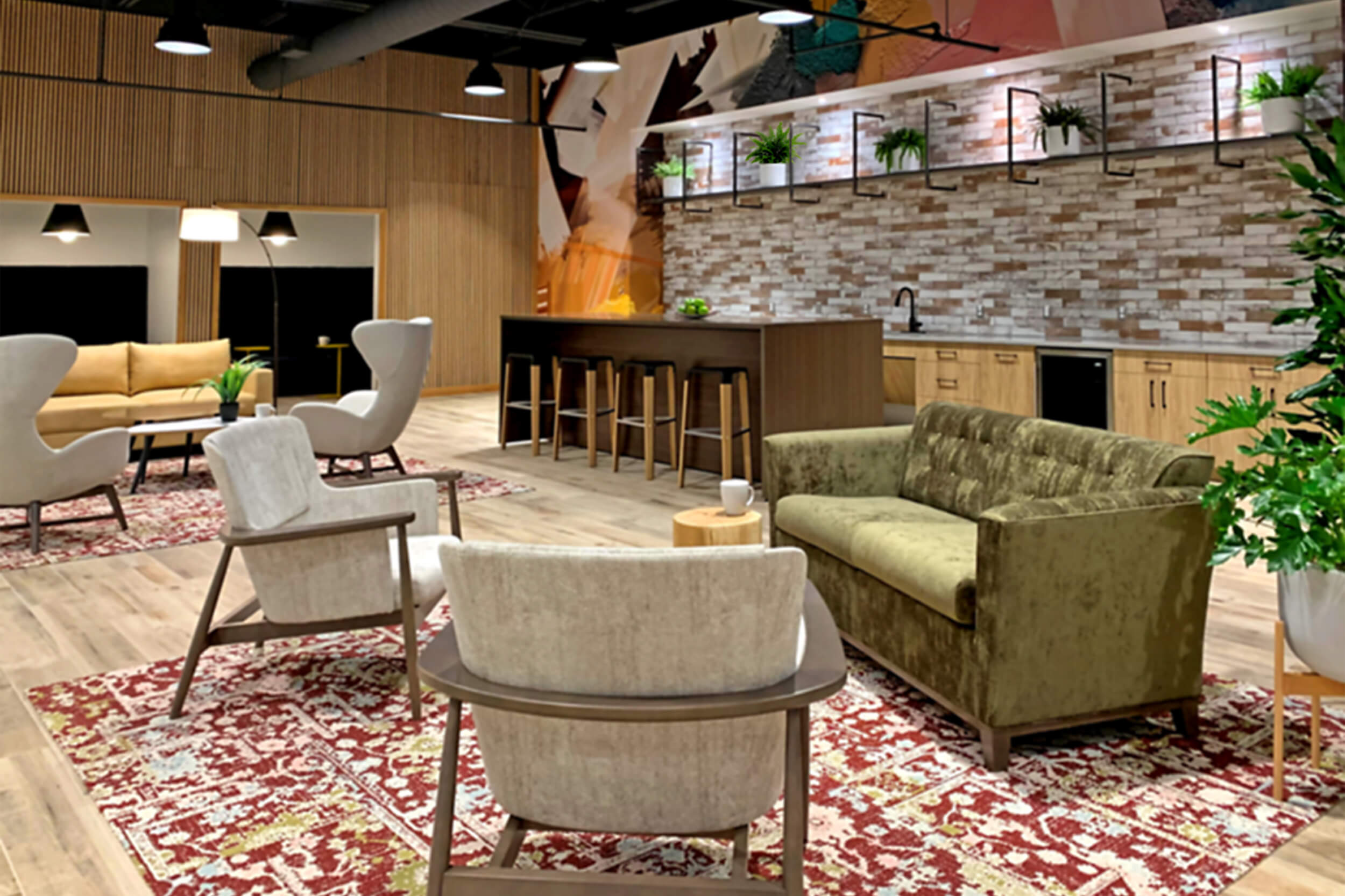 Interior photo of a corporate lounge area. The room features a multicolor carpet, mid-century modern grey and green seats and couch, and a back tiled wall with a wooden work bar area.