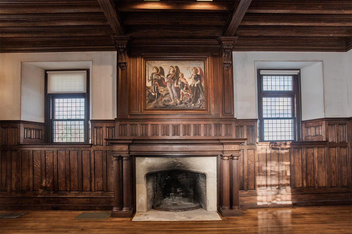 Interior photo of a fireplace in a historical building. The room features dark wood paneling, and above the fireplace there is a painting.