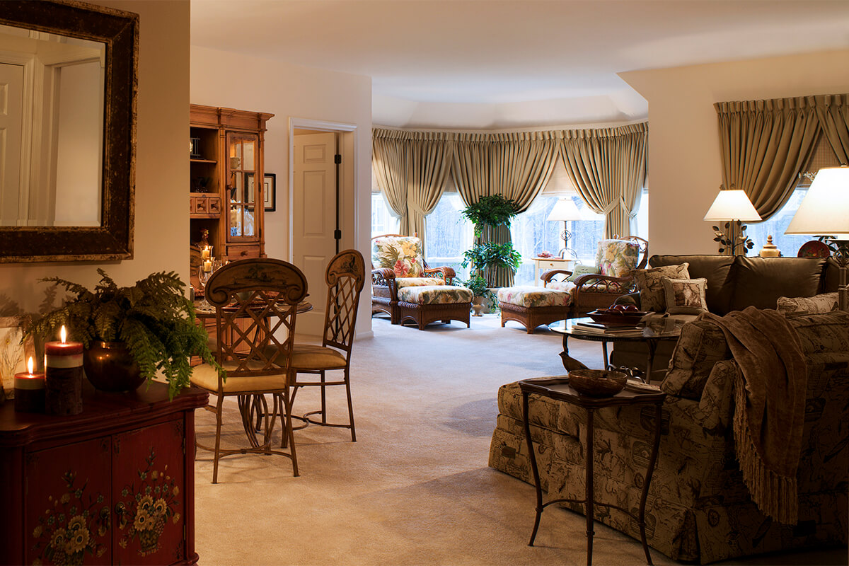 Interior photo showing a resident unit at a senior living facility. The neutral colored room features flower patterned upholstered couches and seating.