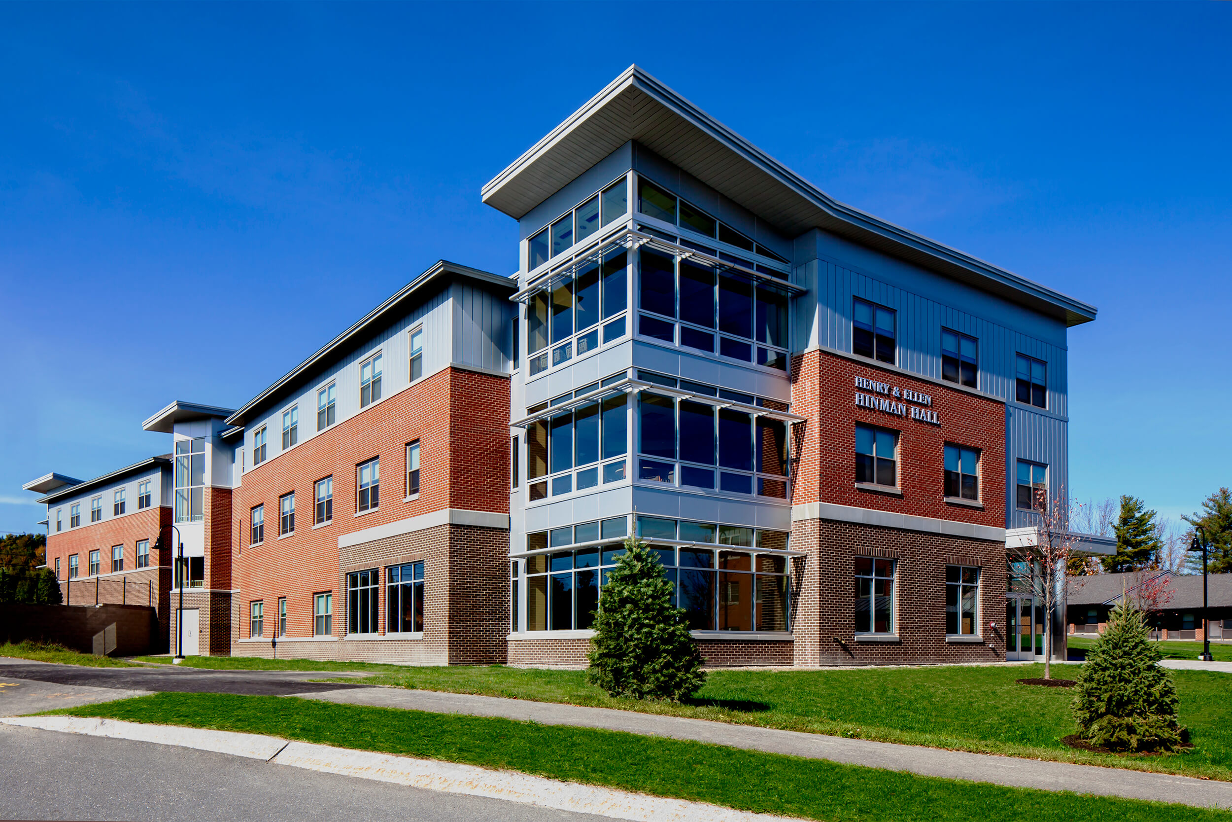 Exterior daytime photo of a college campus student residence building. The building features multiple stories and a brick facade with the axis corner having large glass windows.